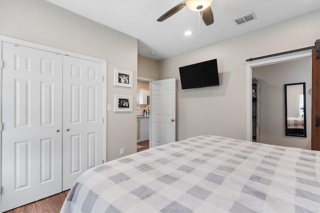 bedroom featuring a barn door, ceiling fan, a closet, and hardwood / wood-style floors