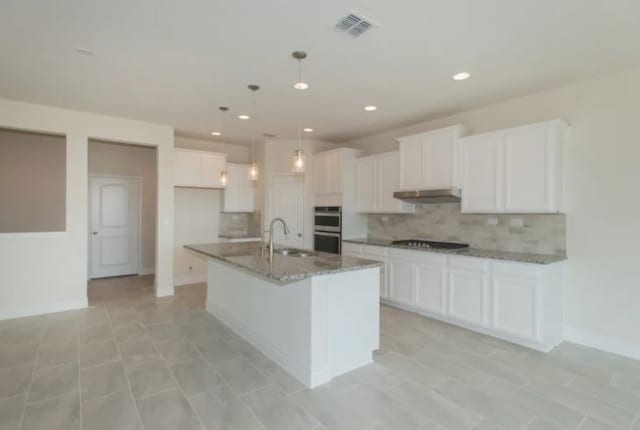 kitchen with white cabinets, decorative backsplash, and an island with sink