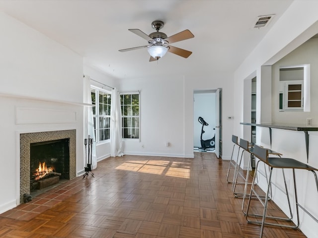 unfurnished living room with a tile fireplace, dark parquet floors, and ceiling fan