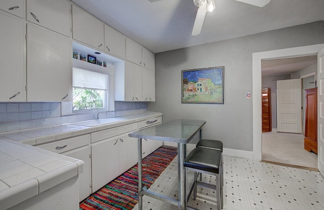 kitchen featuring ceiling fan, tile counters, sink, decorative backsplash, and white cabinets