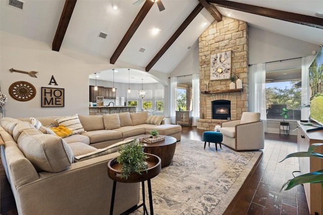 living room with ceiling fan with notable chandelier, high vaulted ceiling, dark hardwood / wood-style flooring, a stone fireplace, and beamed ceiling