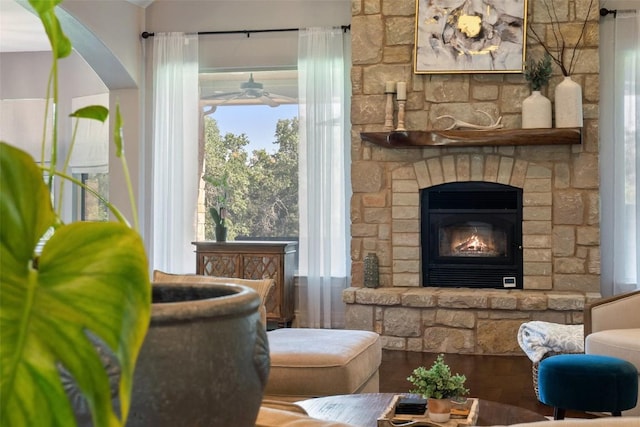 living area featuring a healthy amount of sunlight, ceiling fan, wood finished floors, and a stone fireplace