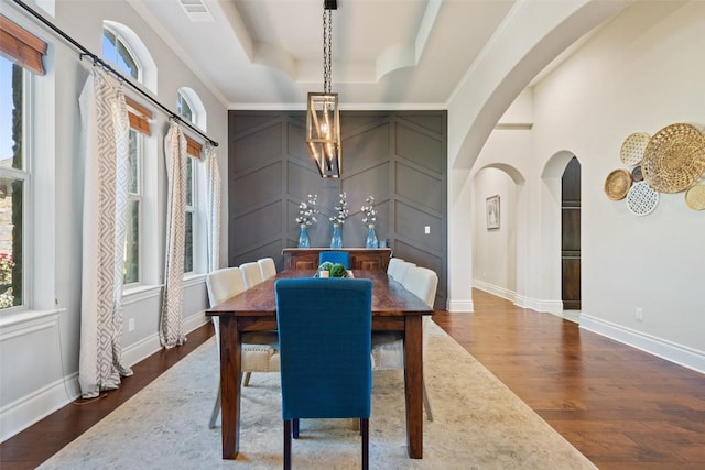 dining space featuring arched walkways, wood finished floors, a raised ceiling, and visible vents