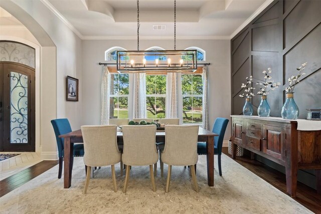 dining room with hardwood / wood-style floors, an inviting chandelier, a raised ceiling, and crown molding