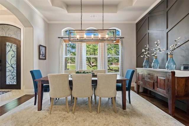 dining room with arched walkways, a raised ceiling, wood finished floors, and ornamental molding