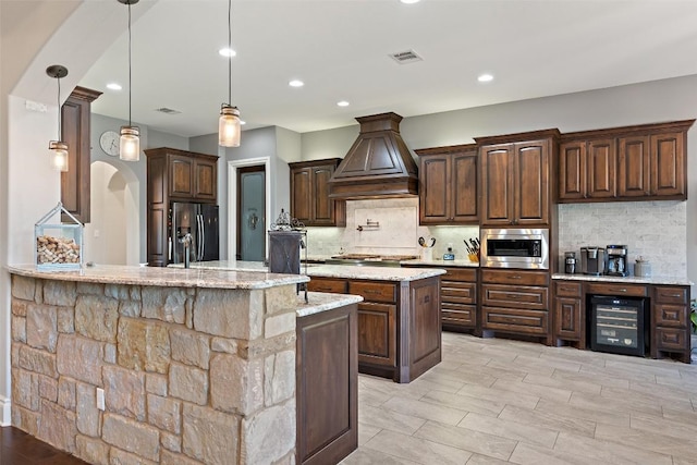 kitchen featuring custom exhaust hood, visible vents, decorative backsplash, appliances with stainless steel finishes, and beverage cooler