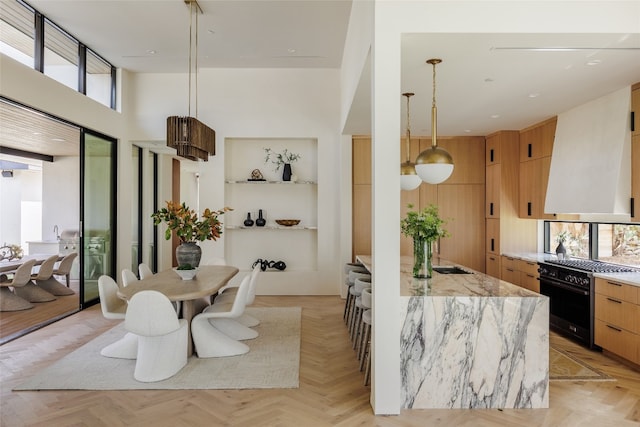 kitchen featuring high end black range oven, hanging light fixtures, light parquet floors, light stone countertops, and custom range hood