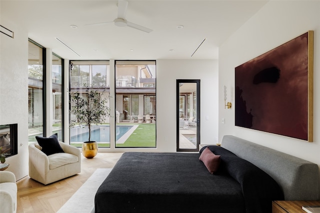 bedroom with light parquet floors, access to outside, ceiling fan, and a wall of windows