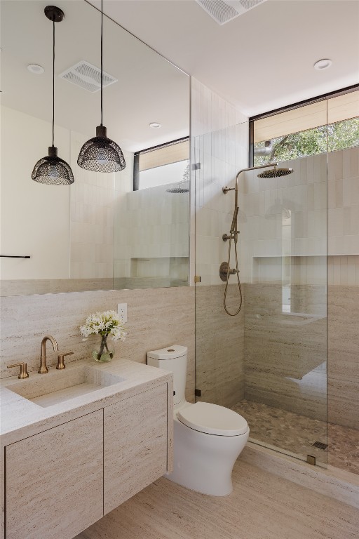 bathroom featuring a tile shower, a wealth of natural light, toilet, and tile walls