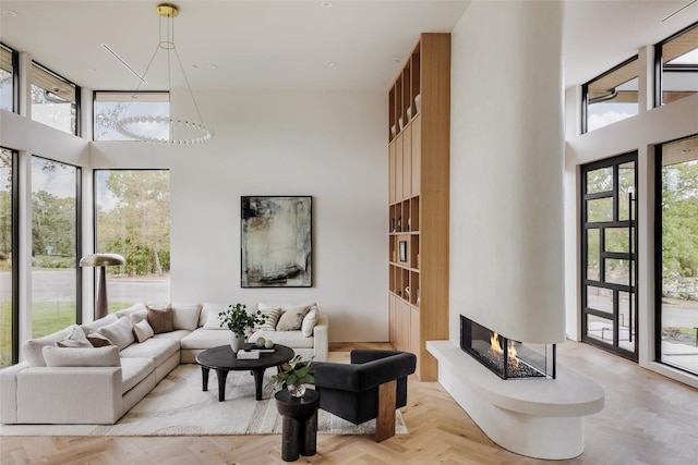 living room with a multi sided fireplace, light parquet flooring, and a high ceiling