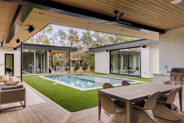 view of pool featuring area for grilling, a wooden deck, ceiling fan, and an outdoor kitchen