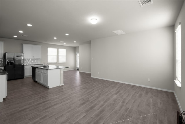 kitchen with stainless steel refrigerator with ice dispenser, decorative backsplash, an island with sink, white cabinetry, and wood-type flooring