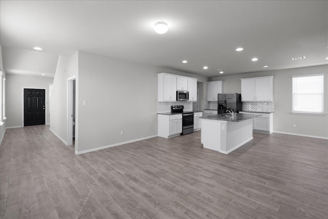 kitchen featuring white cabinetry, light hardwood / wood-style floors, decorative backsplash, a center island with sink, and appliances with stainless steel finishes