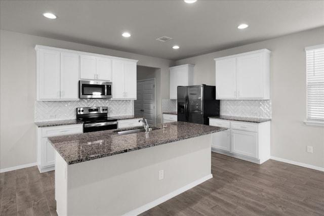 kitchen with white cabinets, dark stone countertops, light wood-type flooring, an island with sink, and stainless steel appliances