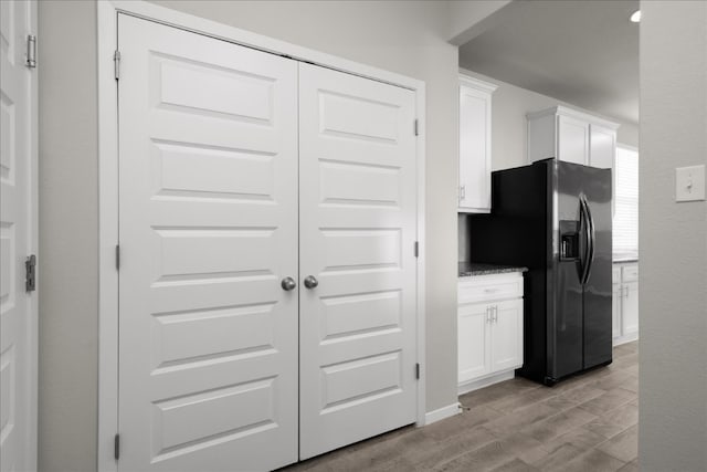 kitchen featuring white cabinets, light hardwood / wood-style flooring, black refrigerator with ice dispenser, and light stone countertops