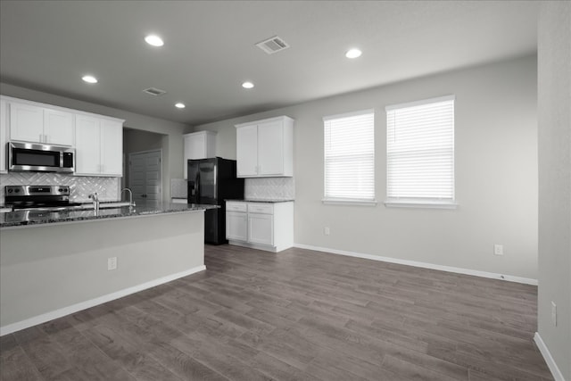 kitchen featuring white cabinets, appliances with stainless steel finishes, tasteful backsplash, stone countertops, and wood-type flooring