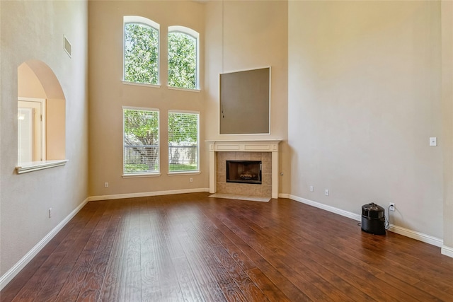 unfurnished living room with a towering ceiling, a tiled fireplace, and dark hardwood / wood-style floors