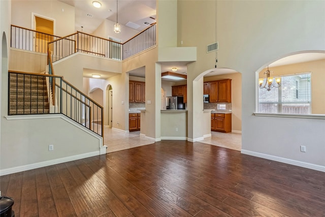 unfurnished living room featuring a high ceiling, light hardwood / wood-style flooring, and an inviting chandelier