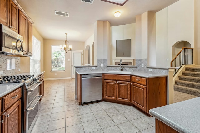 kitchen featuring stainless steel appliances, sink, light tile patterned floors, pendant lighting, and a notable chandelier