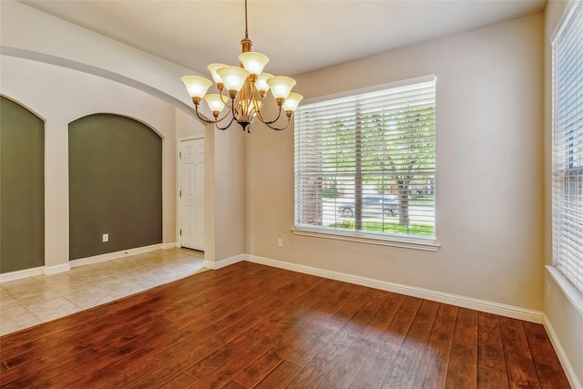 spare room featuring wood-type flooring and a chandelier