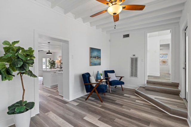 sitting room with ceiling fan, beamed ceiling, and light wood-type flooring