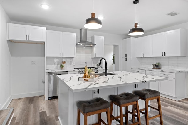 kitchen with white cabinets, a kitchen island with sink, light stone countertops, and wall chimney range hood