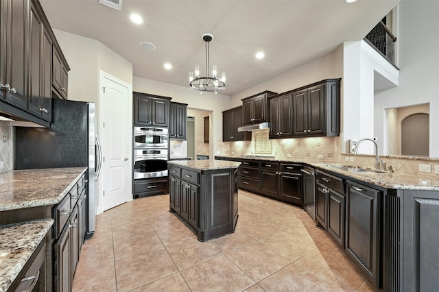 kitchen with light stone countertops, a center island, sink, and hanging light fixtures