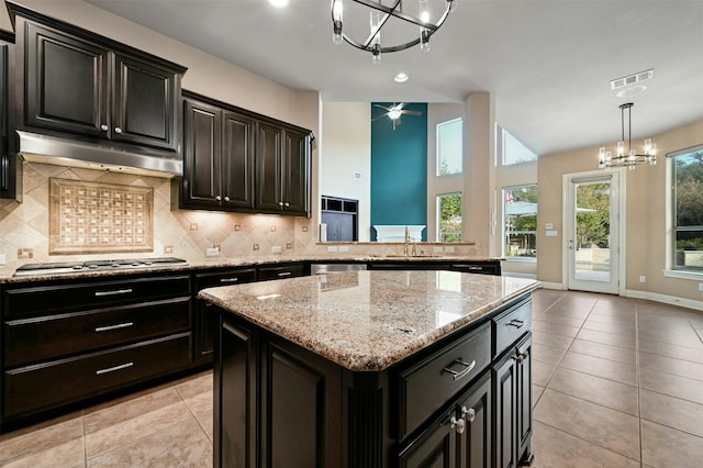 kitchen with appliances with stainless steel finishes, hanging light fixtures, a kitchen island, decorative backsplash, and a chandelier