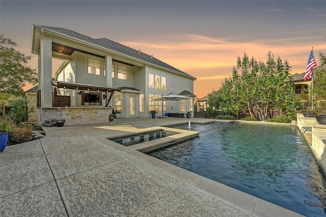 back house at dusk featuring a swimming pool with hot tub, pool water feature, and a patio area