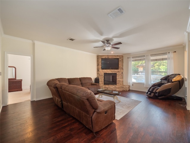 living room featuring ceiling fan, a stone fireplace, ornamental molding, and dark wood-type flooring