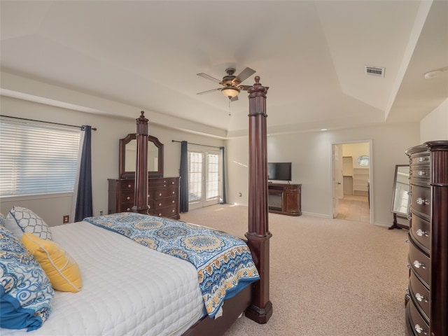 carpeted bedroom featuring a raised ceiling, connected bathroom, and ceiling fan