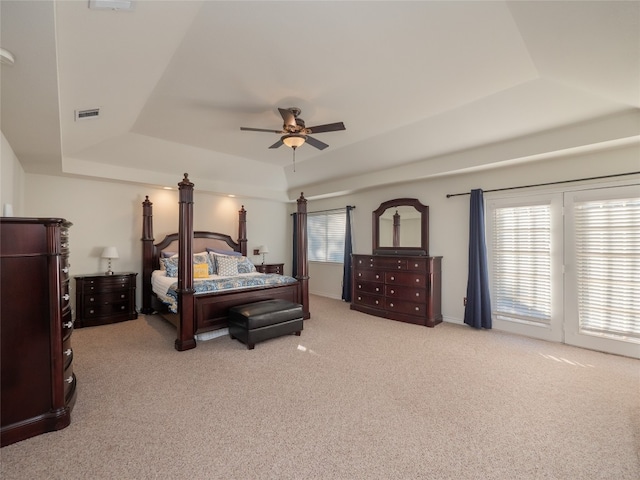 carpeted bedroom featuring a tray ceiling, multiple windows, and ceiling fan