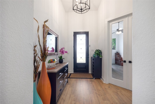 entrance foyer with light hardwood / wood-style flooring, a high ceiling, and ceiling fan with notable chandelier