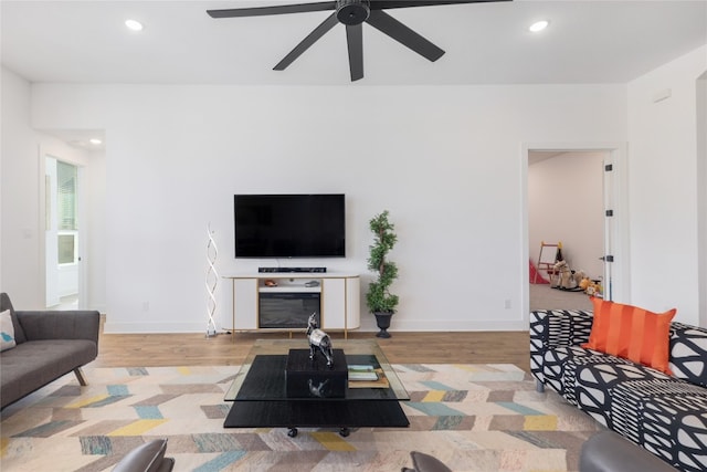 living room featuring ceiling fan, a fireplace, and light wood-type flooring