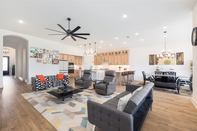 living room featuring ceiling fan with notable chandelier, light hardwood / wood-style floors, and sink