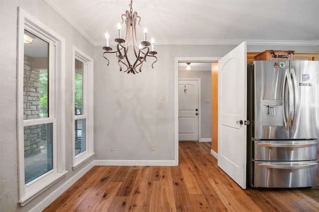 unfurnished dining area with hardwood / wood-style flooring, crown molding, and an inviting chandelier