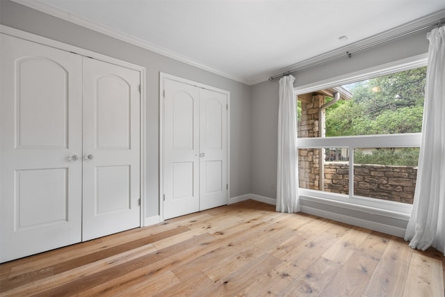 unfurnished bedroom featuring light hardwood / wood-style flooring, multiple closets, and ornamental molding