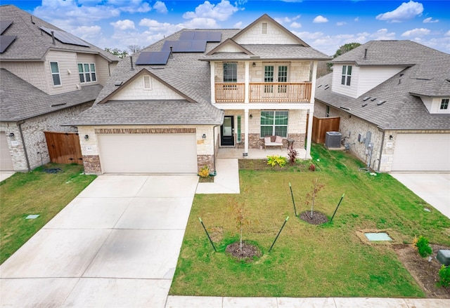 view of front of home with solar panels, central air condition unit, a front yard, a balcony, and a garage