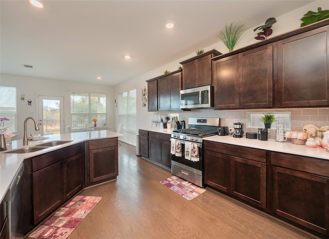 kitchen with appliances with stainless steel finishes, backsplash, dark brown cabinetry, sink, and light hardwood / wood-style flooring