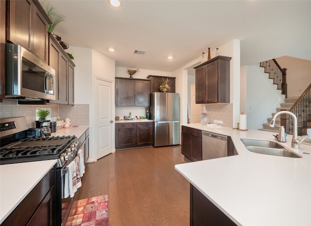 kitchen featuring appliances with stainless steel finishes, backsplash, dark brown cabinetry, sink, and dark hardwood / wood-style floors