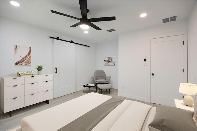 bedroom featuring ceiling fan, a barn door, and light wood-type flooring