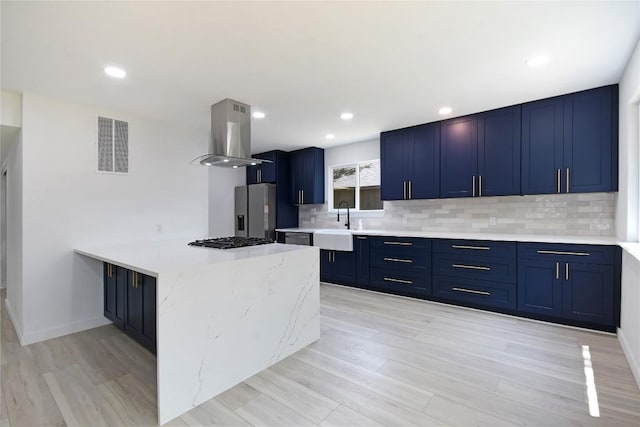 kitchen with blue cabinets, sink, island range hood, appliances with stainless steel finishes, and decorative backsplash