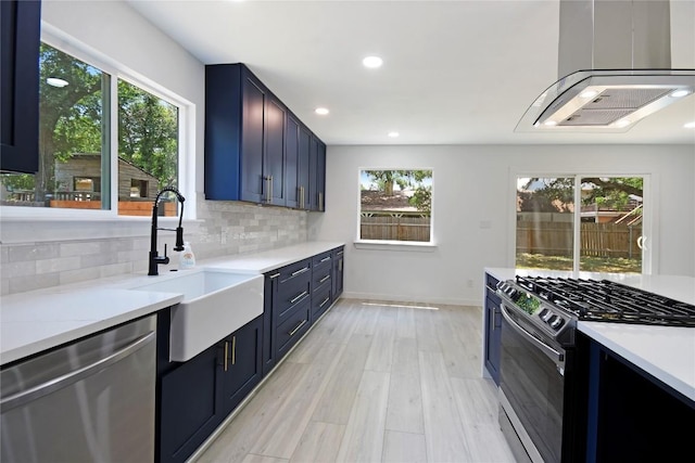 kitchen with appliances with stainless steel finishes, blue cabinets, sink, backsplash, and light hardwood / wood-style flooring