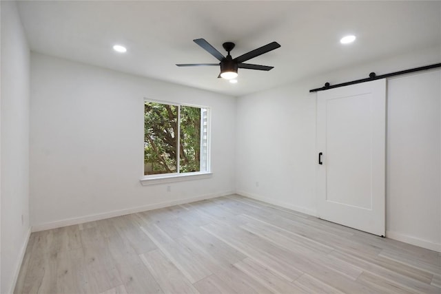 unfurnished bedroom with ceiling fan, a barn door, and light hardwood / wood-style floors