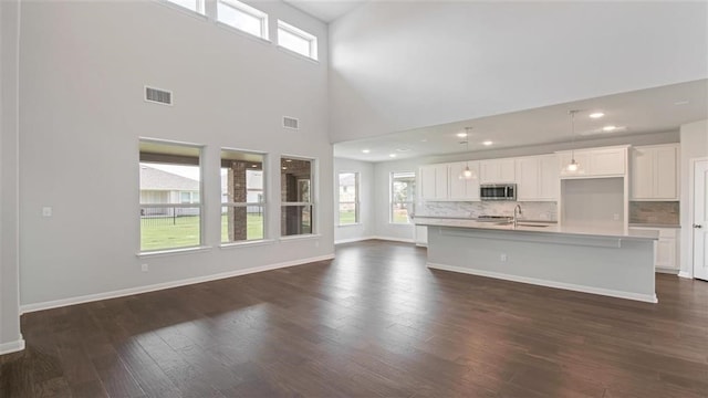 unfurnished living room featuring a towering ceiling, dark hardwood / wood-style flooring, a healthy amount of sunlight, and sink