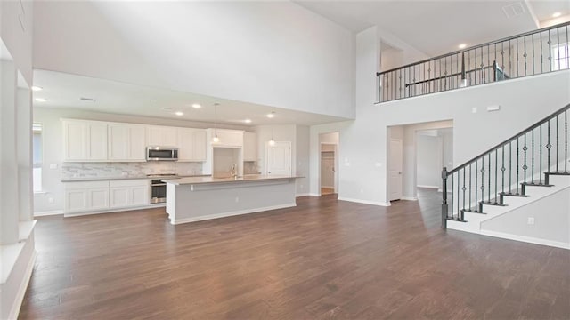 unfurnished living room featuring a towering ceiling, dark wood-type flooring, and sink