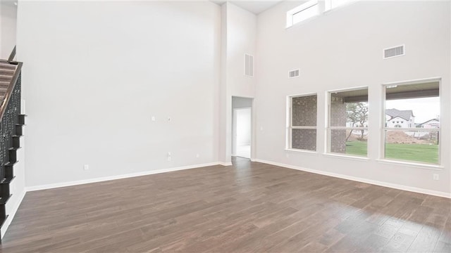 unfurnished living room featuring a towering ceiling and dark hardwood / wood-style floors