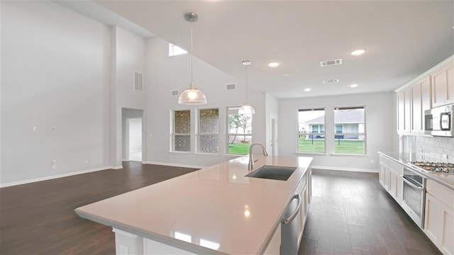 kitchen featuring dark hardwood / wood-style flooring, stainless steel appliances, white cabinetry, hanging light fixtures, and an island with sink