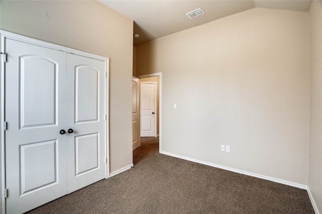 unfurnished bedroom featuring a closet, vaulted ceiling, and dark colored carpet