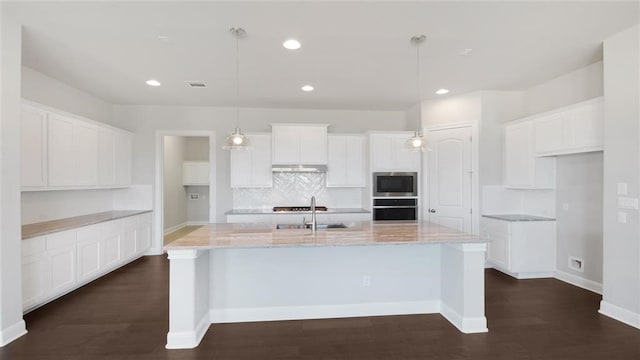 kitchen with white cabinets, decorative light fixtures, stainless steel appliances, and a kitchen island with sink